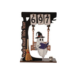 A Halloween-themed wooden desk calendar featuring a flip-count display showing 6, 9, and 7, with a ghost on a swing reading a book, a broomstick, a vertical 'Books Read This Year' plaque, and a small skull on a white background.