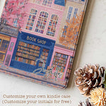 Design for a Kindle softcolor case featuring an illustration of a pink building with a blue roof and white-framed windows. In front, a bookshelf labeled 'BOOK SHOP' is displayed.