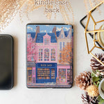 Design for a Kindle softcolor case featuring an illustration of a pink building with a blue roof and white-framed windows. In front, a bookshelf labeled 'BOOK SHOP' is displayed.