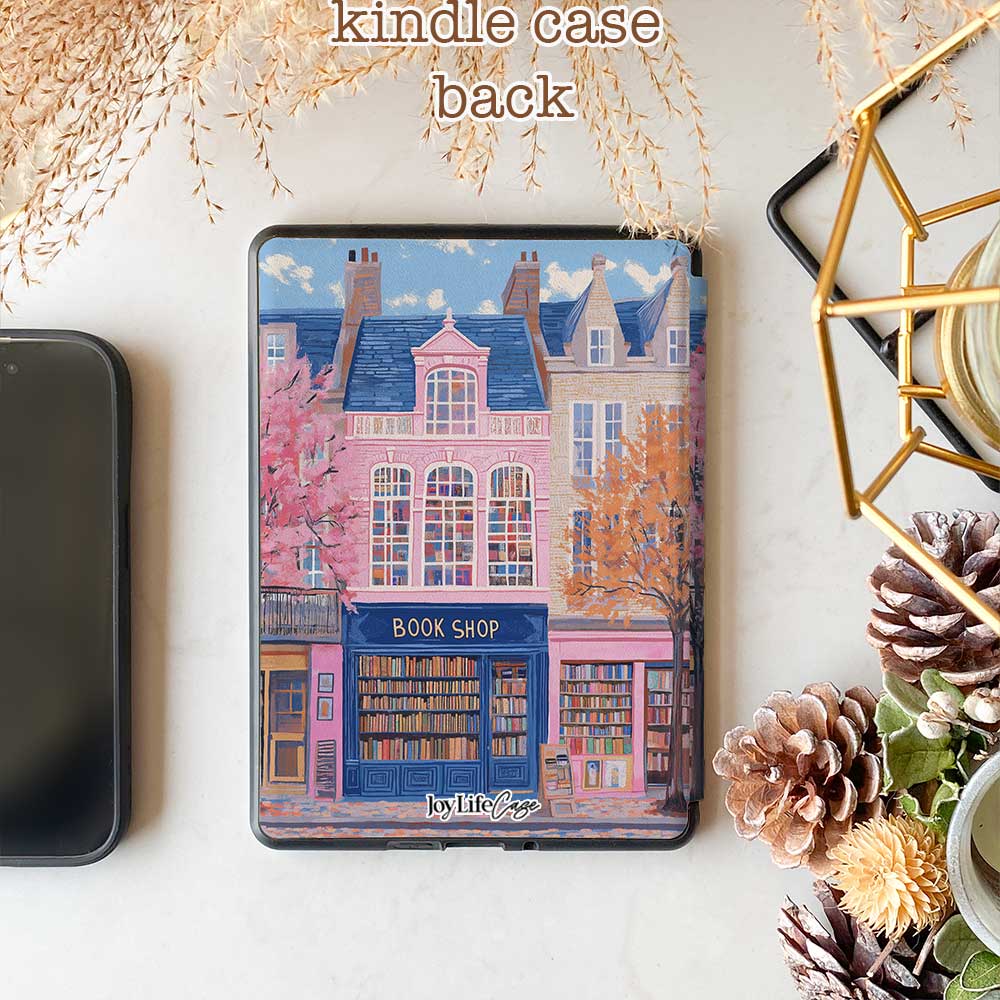 Design for a Kindle softcolor case featuring an illustration of a pink building with a blue roof and white-framed windows. In front, a bookshelf labeled 'BOOK SHOP' is displayed.