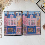 Design for a Kindle softcolor case featuring an illustration of a pink building with a blue roof and white-framed windows. In front, a bookshelf labeled 'BOOK SHOP' is displayed.