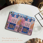 The iPad Pro M4 Case design features an illustration of a city street with vibrant buildings. The most prominent is a pink building in the center, labeled "BOOK SHOP." Large windows on the building display colorful bookshelves, creating an atmosphere full of knowledge and culture.